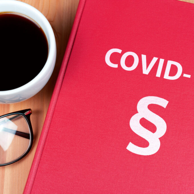 Czerwona książka z paragrafem i napisem COVID-19, okulary i kawa