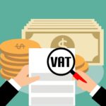Dłonie z lupą nad fakturą z napisem VAT i monetami