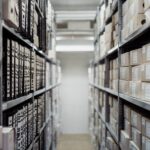 Korytarz archiwum z regałami pełnymi segregatorów